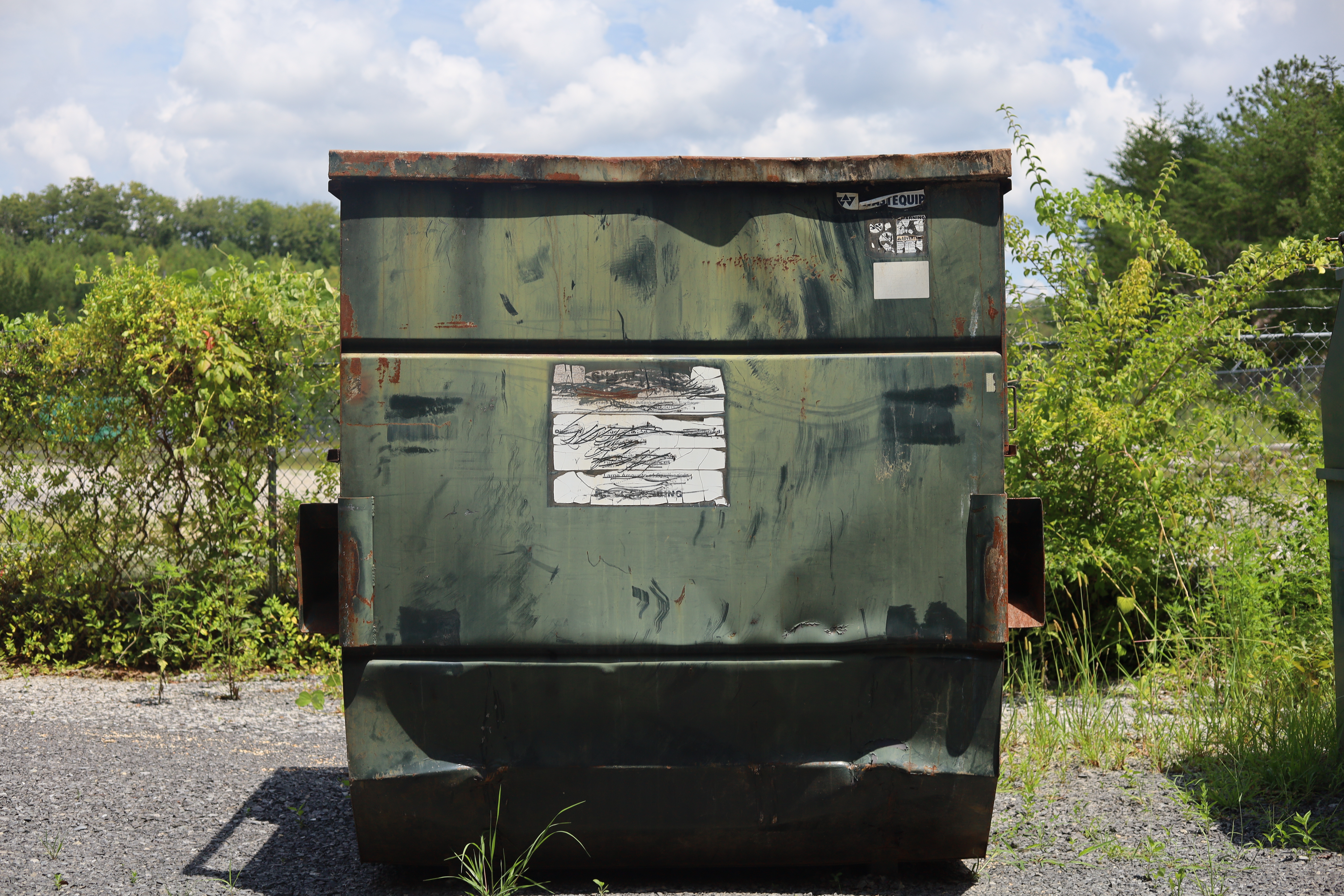 Worn, rusted front-load dumpster before Trident reconditioning